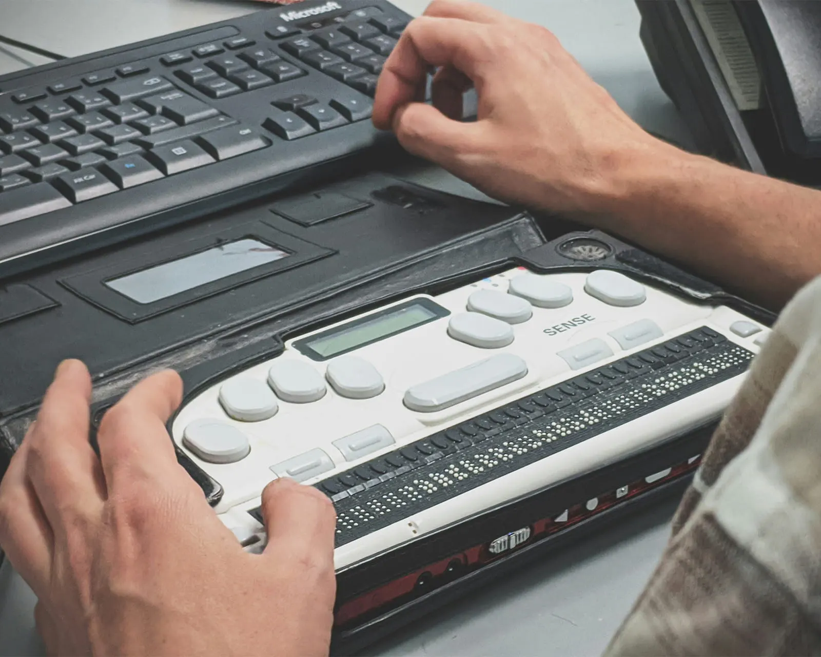 A person reading a refreshable braille display connected to a computer keyboard