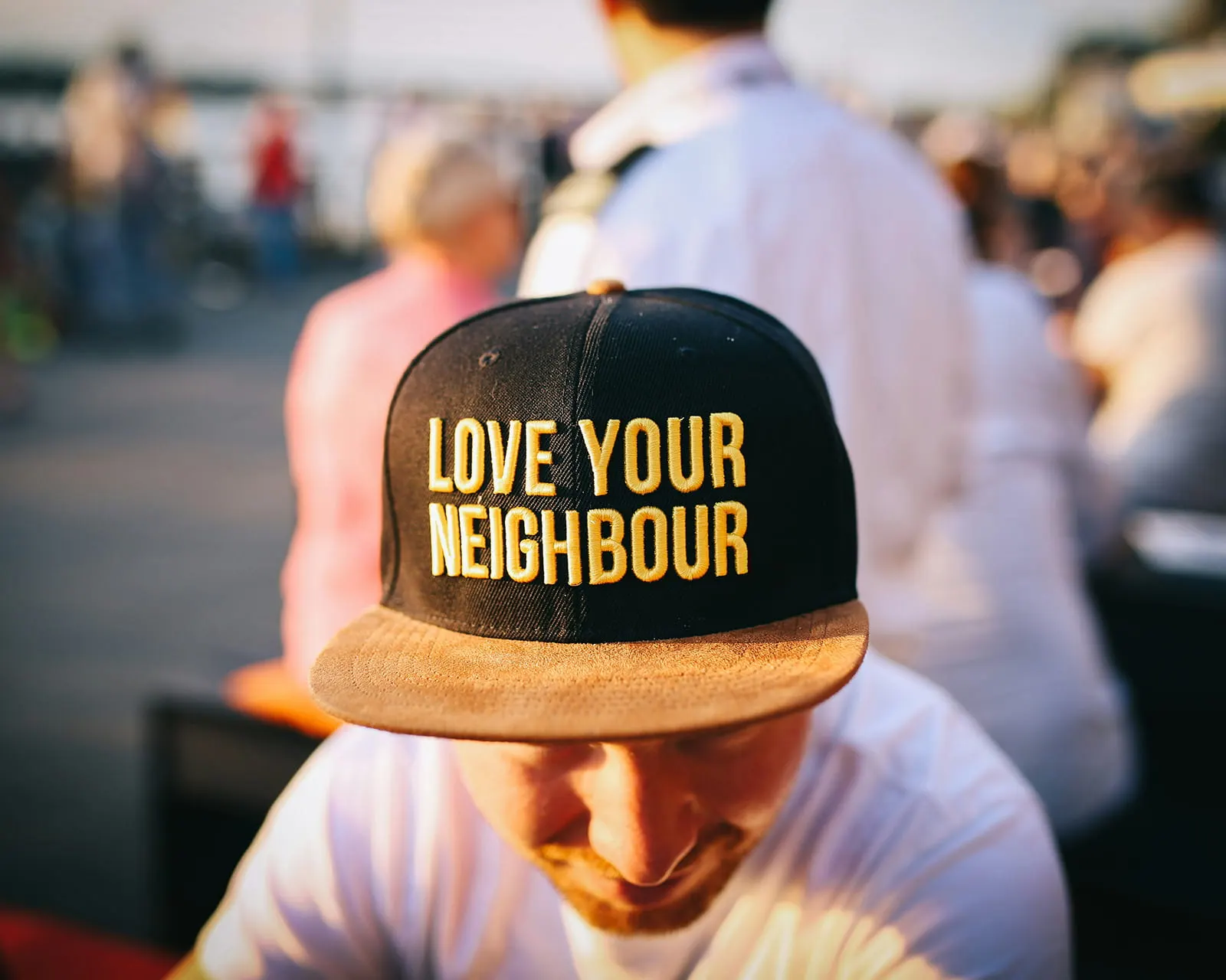 A man at an outdoor community event wearing a cap that reads “Love Your Neighbour”